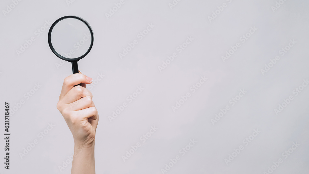 Searching glass. Zooming loupe. Female hand examining copy space with magnifying equipment exploring isolated on gray background. Searching glass. Zooming loupe. Female hand examining copy space with magnifying equipment exploring isolated on gray background.