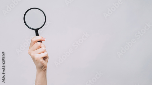 Searching glass. Zooming loupe. Female hand examining copy space with magnifying equipment exploring isolated on gray background.