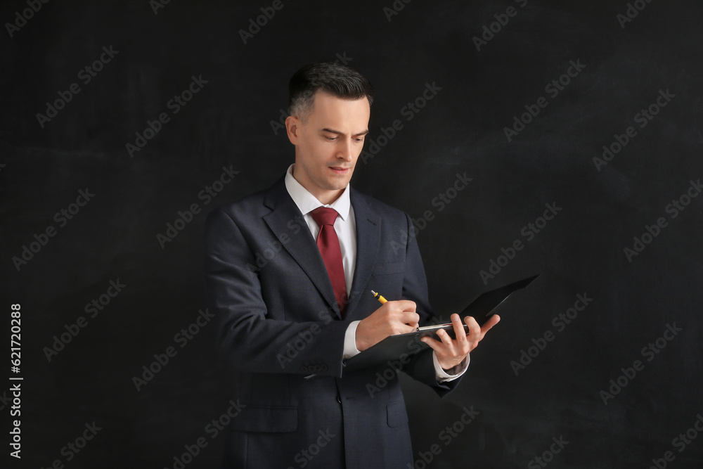 Male teacher writing in clipboard near blackboard in classroom Male teacher writing in clipboard near blackboard in classroom