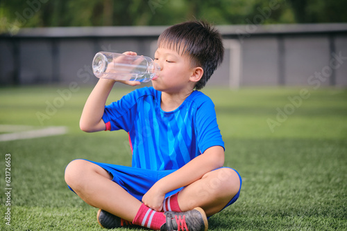 Asian boy child in soccer uniform drinking pure water from reusable water bottle after playing football at Training Session, Soccer Drills for Kids, Kid drink water after exercise, Zero waste concept