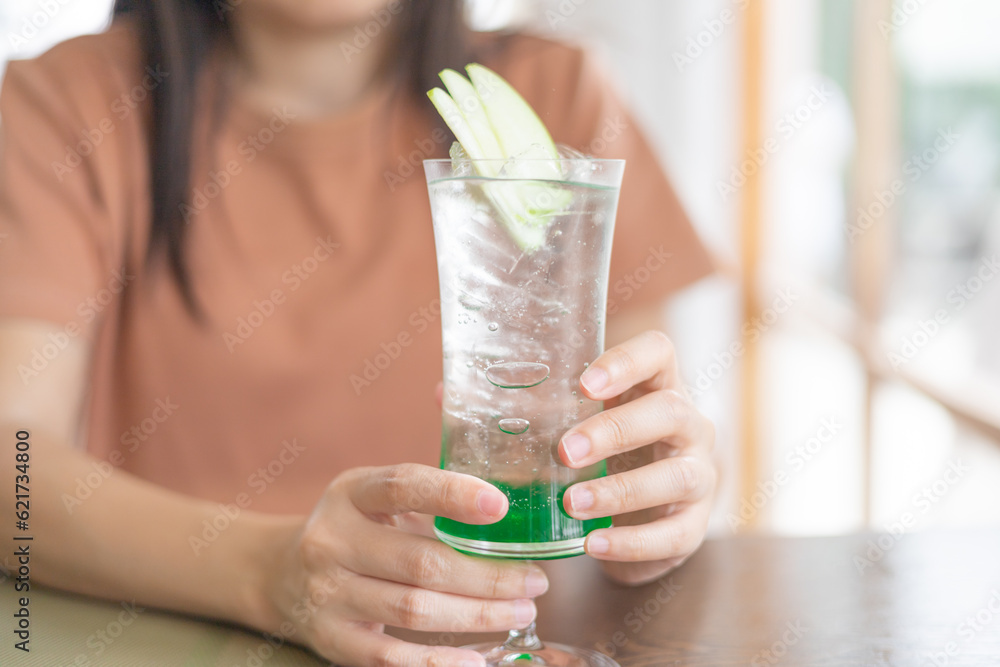 Fototapeta premium Close-up a hand of Young Asian woman hold a drinking green apple juice in the restaurant. spending time in cafeteria. healthy drink. enjoy eating. spending time in cafeteria.