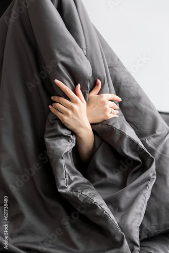 Hands of woman is lying in bed and hiding under dark grey blanket. Doesn't want to wake up. Lack of sleep concept