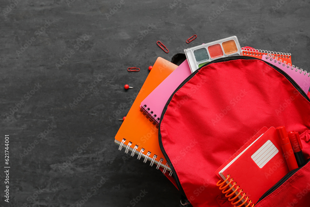 Naklejka premium Red school backpack with notebooks, watercolors and paper clips on black background