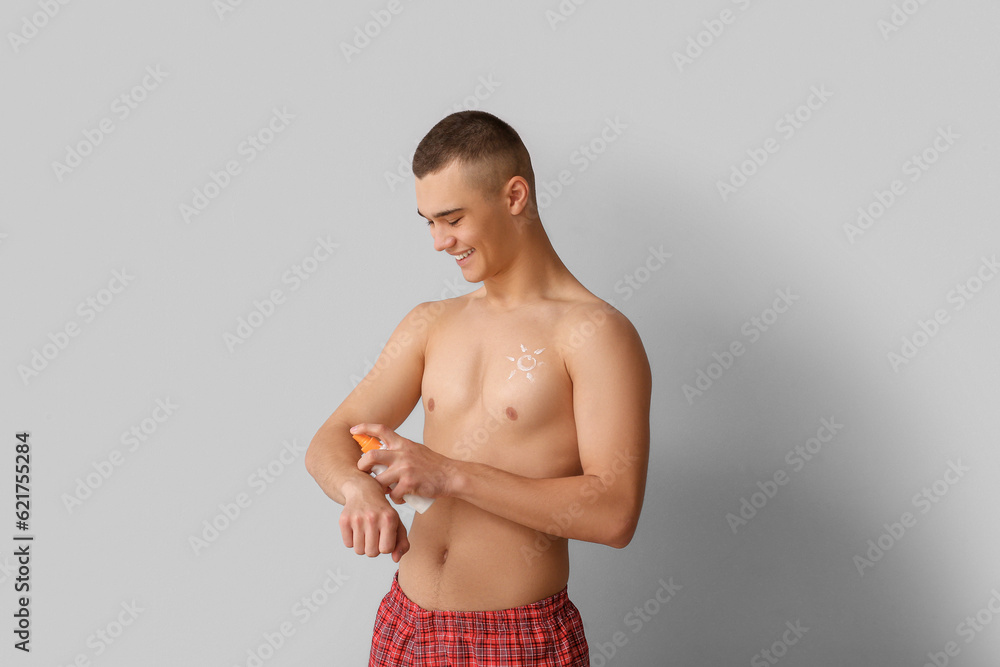 Obraz premium Happy young man applying sunscreen cream on his body against grey background