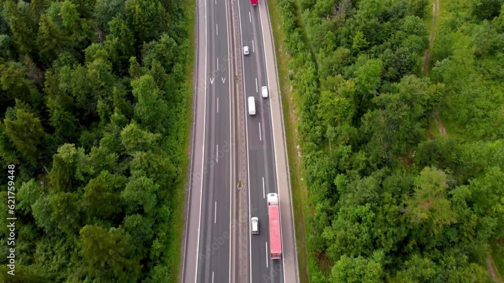 Bird-eye view of European highway with nice traffic flow cars and trucks in the middle of summer with national road in the green belt between tall trees Bird-eye view of European highway with nice traffic flow cars and trucks in the middle of summer with national road in the green belt between tall trees