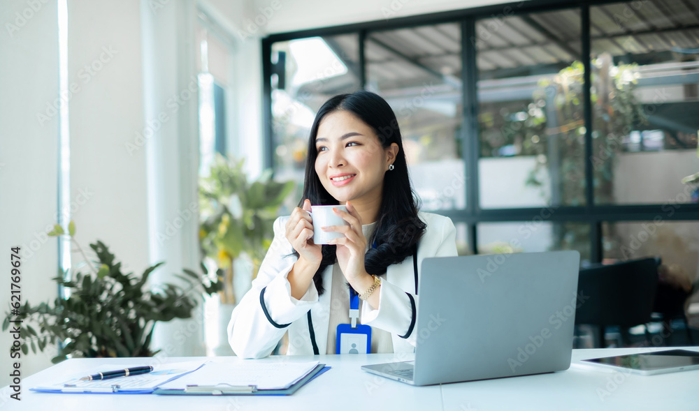 Asian businesswoman smiling happily with a new morning holding a cup of coffee lightly sipping coffee professional woman in size working in the office Asian businesswoman smiling happily with a new morning holding a cup of coffee lightly sipping coffee professional woman in size working in the office