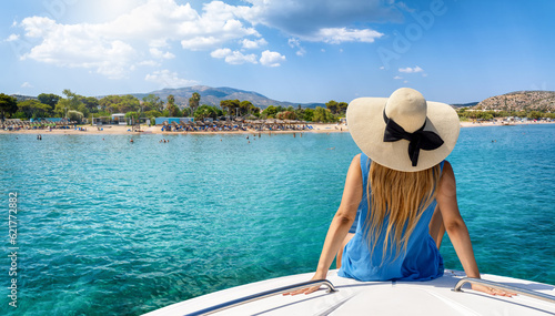 A tourist woman at summer vacation on a boat looks at the beautiful beach of Varkiza, Greece, with turquoise sea and sunshine