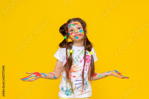 Portrait of a girl with a face painted with multicolored paints. Children's creativity. A happy child stained to the paint. Yellow isolated background.