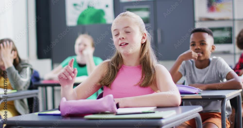 Happy diverse schoolchildren at desks raising hands in school classroom Happy diverse schoolchildren at desks raising hands in school classroom