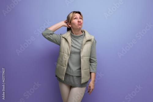dreaming blonde 30s woman in casual vest on studio blue background