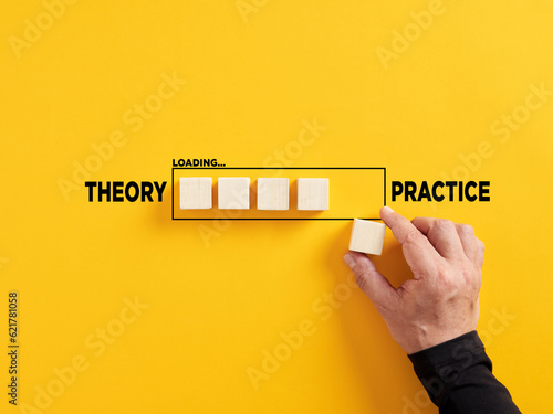 Transition of theory into practice. Implementation of theories in practice. Hand places a wooden cube to the loading bar with the words theory and practice. photo
