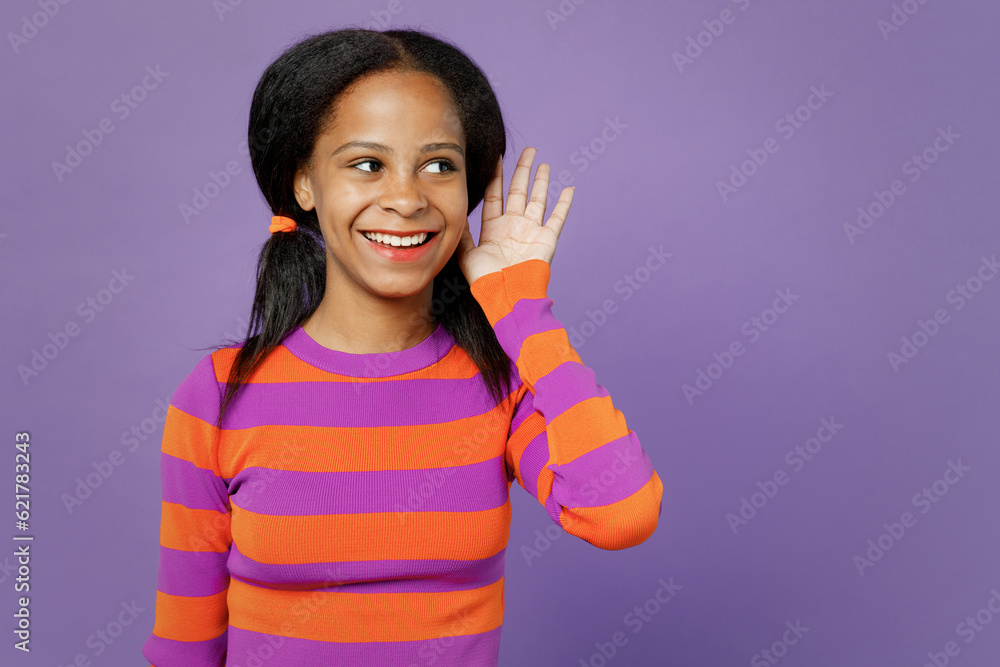 Little kid teen girl of African American ethnicity 15-16 year old wear striped orange sweatshirt try hear you overhear listen intently isolated on plain purple background. Childhood lifestyle concept. Little kid teen girl of African American ethnicity 15-16 year old wear striped orange sweatshirt try hear you overhear listen intently isolated on plain purple background. Childhood lifestyle concept.