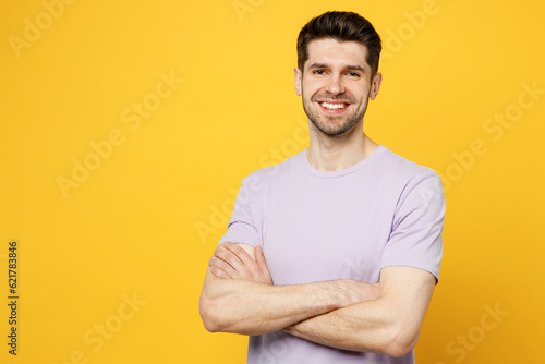 Young smiling happy fun cheerful caucasian man he wear light purple t-shirt casual clothes look camera hold hands crossed folded isolated on plain yellow background studio portrait. Lifestyle concept.