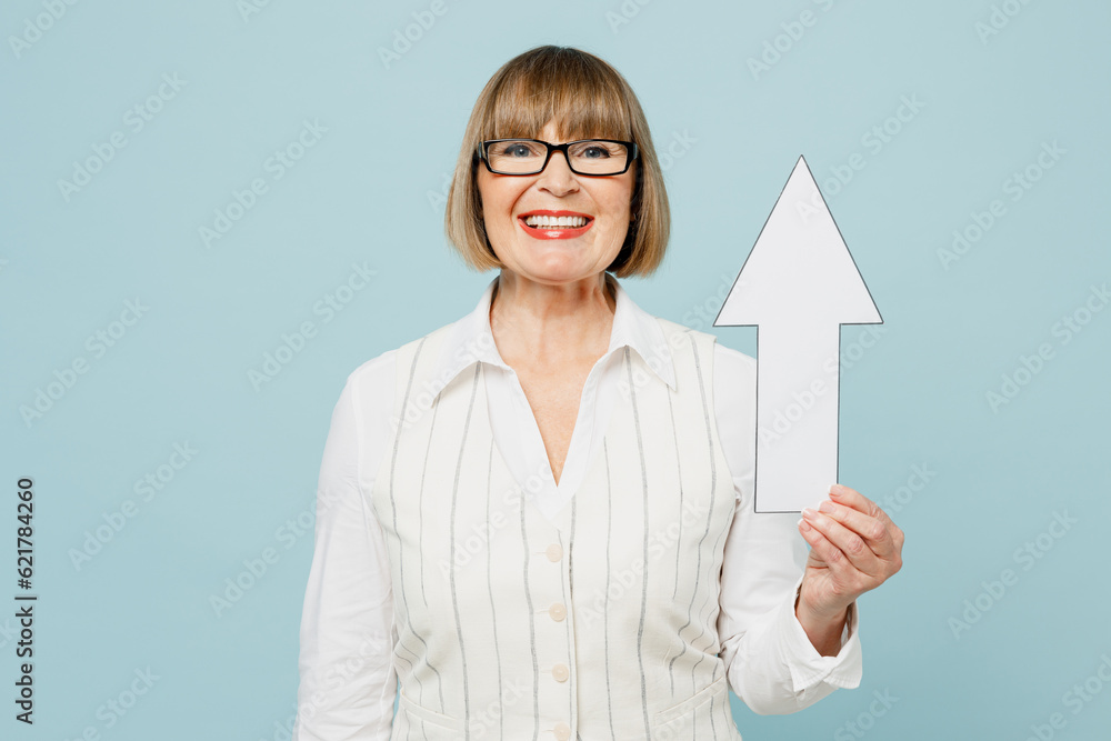 Blonde smiling happy successful employee business woman 50s wear white classic suit glasses formal clothes holding up arrow isolated on plain pastel light blue background. Achievement career concept. Blonde smiling happy successful employee business woman 50s wear white classic suit glasses formal clothes holding up arrow isolated on plain pastel light blue background. Achievement career concept.