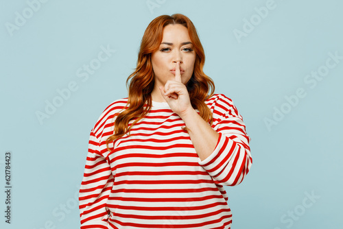 Young secret chubby overweight woman she wearing striped red shirt casual clothes saying hush be quiet with finger on lips shhh gesture isolated on plain pastel light blue background studio portrait. photo