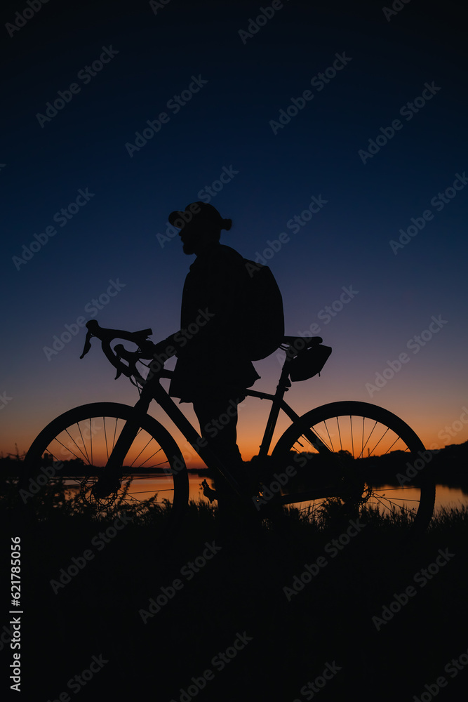 Obraz premium Silhouette of a man with a bicycle enjoying the sunset.