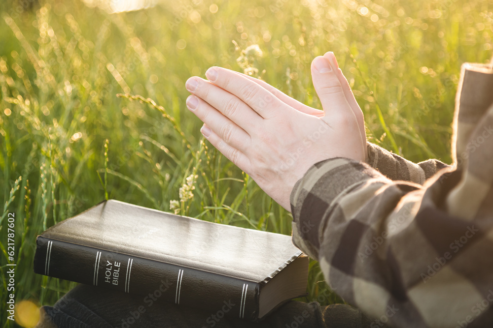 Bible and male hands in a field, concept for faith, spirituality, and religion.
