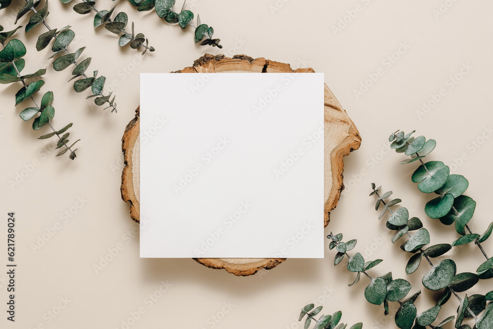 Blank paper sheet card on wooden stand with eucalyptus leaves on beige background. Aesthetic card for wedding, greeting, invitation and branding, logo and design, bohemian style. Top view, flat lay
