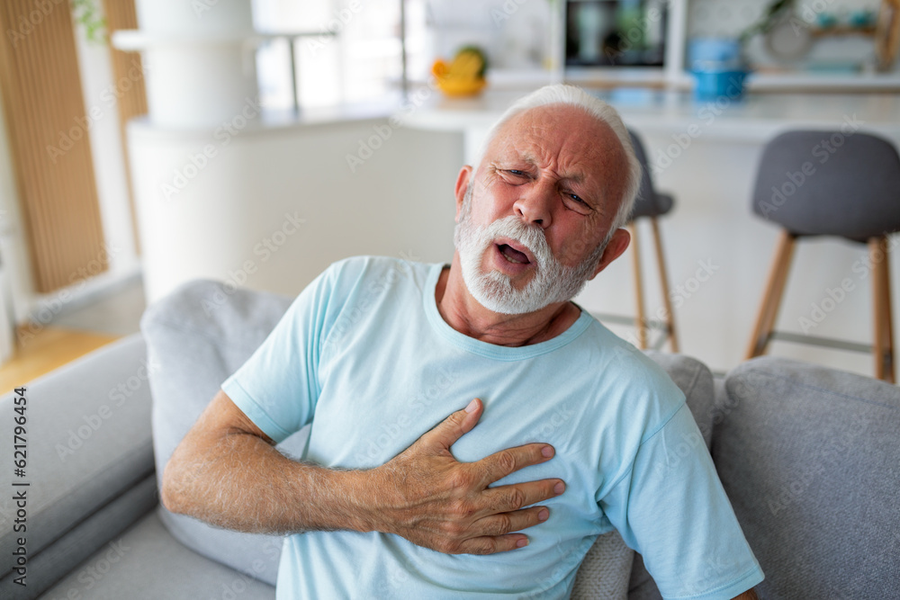Senior man presses hand to chest has heart attack suffers from unbearable pain, Mature man with pain on heart in living room. Senior man suffering from bad pain in his chest heart attack at home Senior man presses hand to chest has heart attack suffers from unbearable pain, Mature man with pain on heart in living room. Senior man suffering from bad pain in his chest heart attack at home