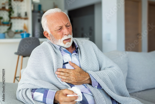 Mature man, visibly unwell, holds his chest in discomfort. The image captures his pain and the need for relief, depicting the experience of illness and the vulnerability of health in this stock photo