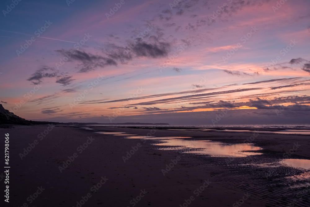 A magnificent capture of a dramatic sunset sky mirrored in the sandy beach and the rhythmic waves of the sea. The breathtaking play of colors creates a truly mesmerizing spectacle, encapsulating the