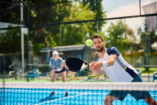 Fotografie Young athletic man plays padel on outdoor tennis court.