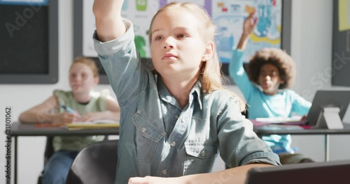 Video of eager caucasian schoolgirl at desk raising hand and answering in diverse class, copy space