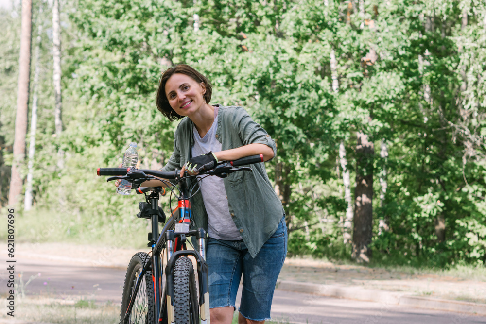 Cyclist have rest and relax, drinking bottle of water for hydrationand for energy. Female wearing casual green jacket jeans riding bicycle bike on bike. Active urban healthy lifestyle cycling concept