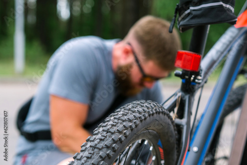 Male hands pumping up a bike tire using small hand pump.
Bearded man repairing bicycle, pumping up tire in nature in summer. People active urban healthy lifestyle cycling concept