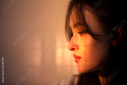 The face of a pensive girl in profile is illuminated by warm light from the window. photo