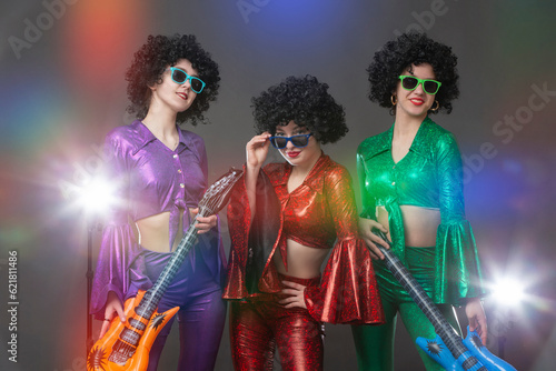 Disco girls in vintage style with toy guitars in the rays of stage light.