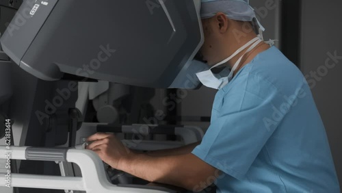 Doctor uses innovative robotic equipment to perform surgery remotely. Process of using stereoscopic monitor to watch and control surgical manipulators in operating room of modern clinic