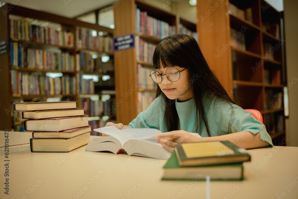 Little girl posing in public library room selecting for reading. girl chooses books on shelves learning from books and notebook is school education benefits of everyday reading concept. Little girl posing in public library room selecting for reading. girl chooses books on shelves learning from books and notebook is school education benefits of everyday reading concept.