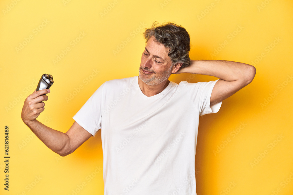 Man holding a razor, yellow studio background touching back of head, thinking and making a choice. Man holding a razor, yellow studio background touching back of head, thinking and making a choice.