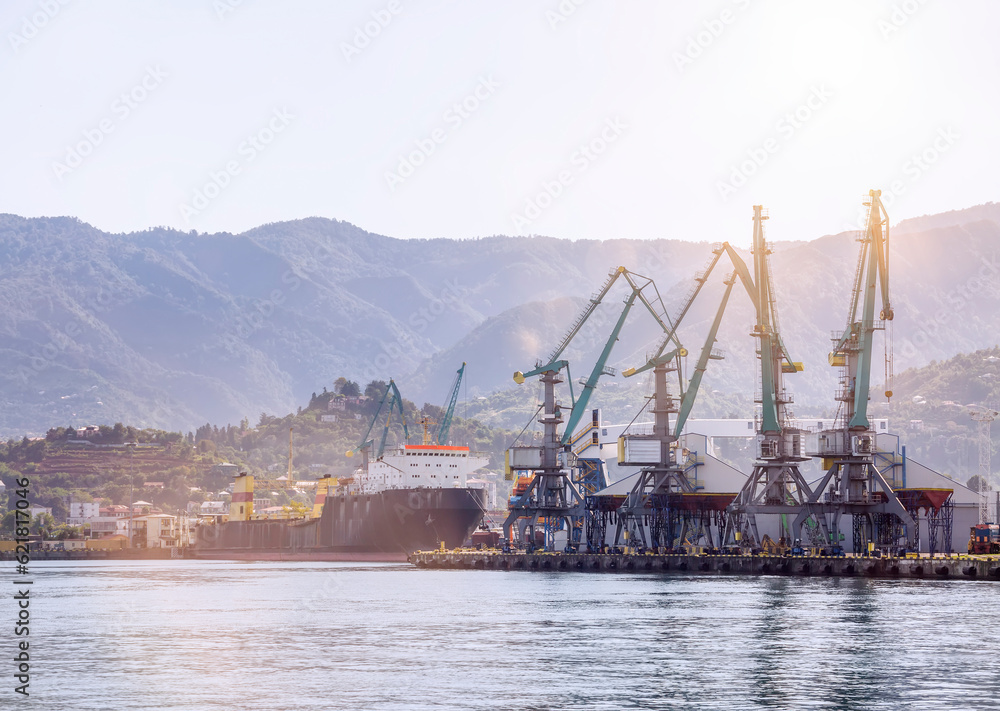 Seascape with loading cranes and a ship against the background of mountains in the rays of the morning sun