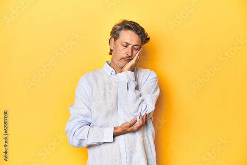 Middle-aged man posing on a yellow backdrop who is bored, fatigued and need a relax day.