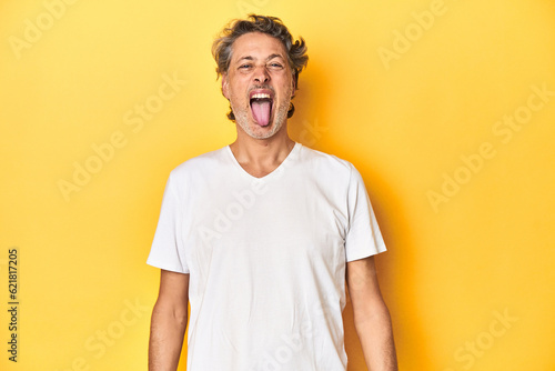 Middle-aged man posing on a yellow backdrop funny and friendly sticking out tongue. © Asier