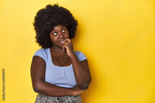 African-American woman with afro, studio yellow background relaxed thinking about something looking at a copy space.