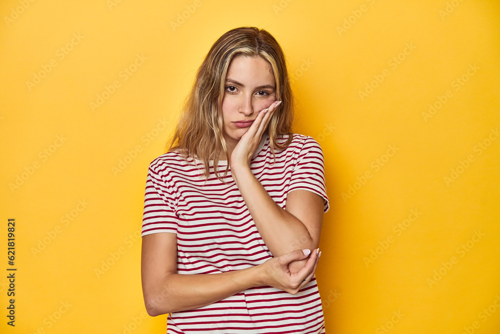 Young blonde Caucasian woman in a red striped t-shirt on a yellow background, who is bored, fatigued and need a relax day. Young blonde Caucasian woman in a red striped t-shirt on a yellow background, who is bored, fatigued and need a relax day.
