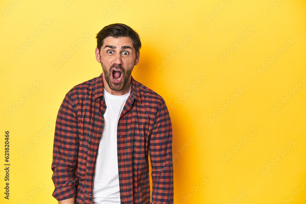 Caucasian man in red checkered shirt, yellow backdrop shouting very angry, rage concept, frustrated. Caucasian man in red checkered shirt, yellow backdrop shouting very angry, rage concept, frustrated.