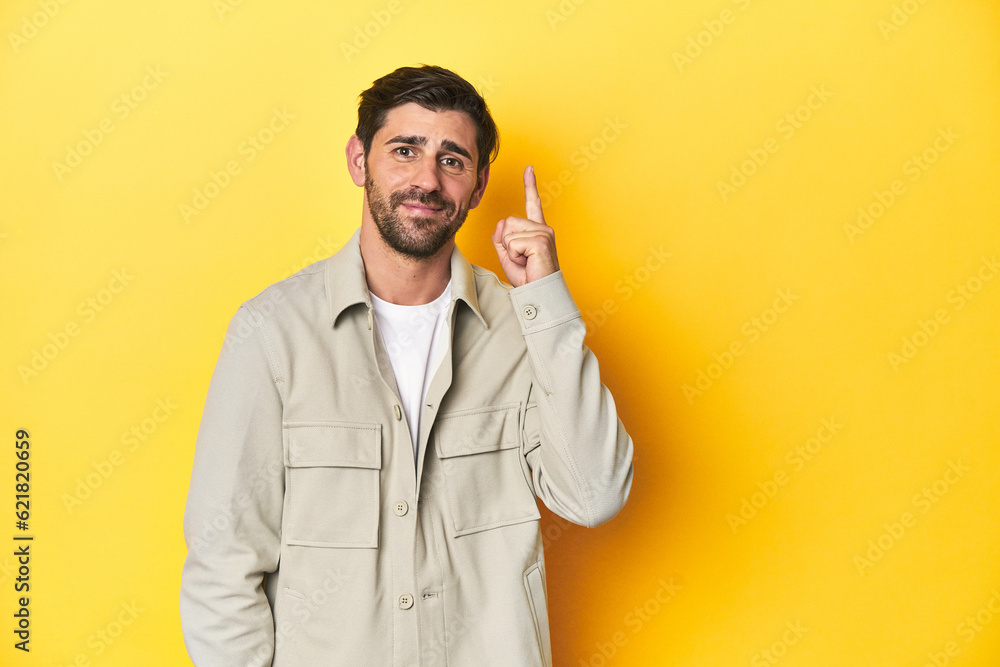 Caucasian man in grey shirt, studio shot on yellow showing number one with finger. Caucasian man in grey shirt, studio shot on yellow showing number one with finger.
