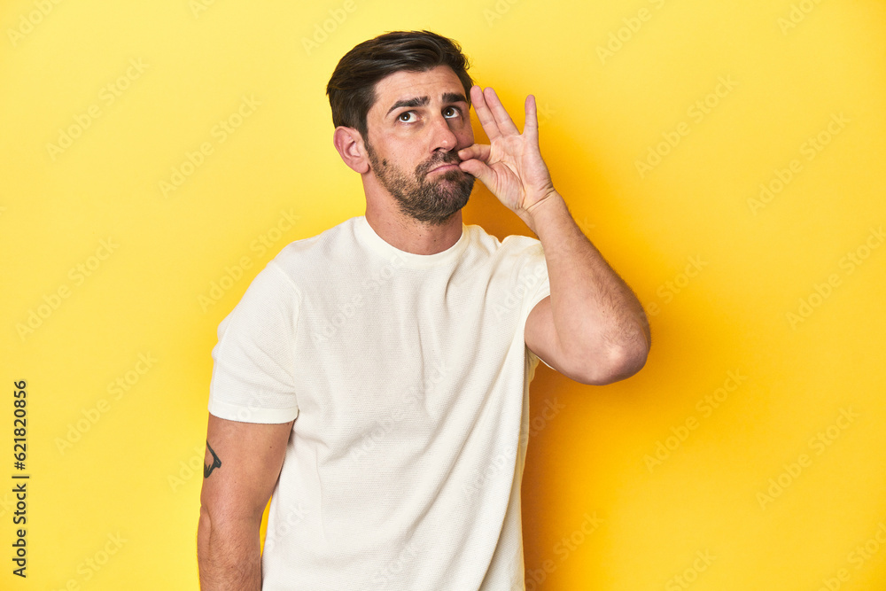 Caucasian man in white t-shirt on yellow studio background with fingers on lips keeping a secret. Caucasian man in white t-shirt on yellow studio background with fingers on lips keeping a secret.