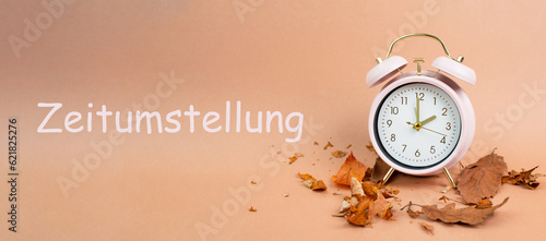 Alarm clock with autumn foliage, end of daylight saving time in fall, winter time changeover stands in german language beside the clock
 photo