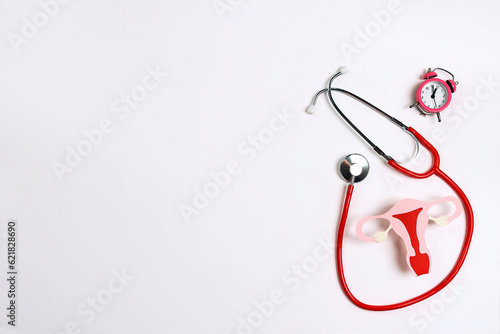 Women's health awareness concept. Uterus symbol with stethoscope and alarm clock on white background. photo