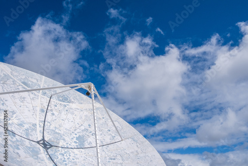 View of a large satellite dish to observe the cosmos, decorated with the lunar topography, with large white clouds in the background. photo