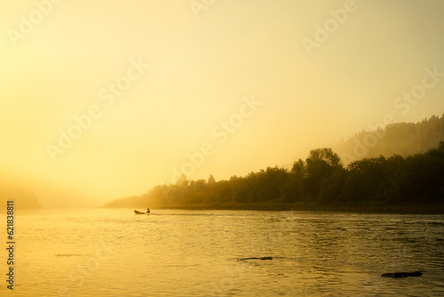 Fototapeta Naklejka Na Ścianę i Meble -  A fishing motor boat moves along the calm surface of a mountain river in the rays of the setting sun. Golden sunset on the river. High quality photo