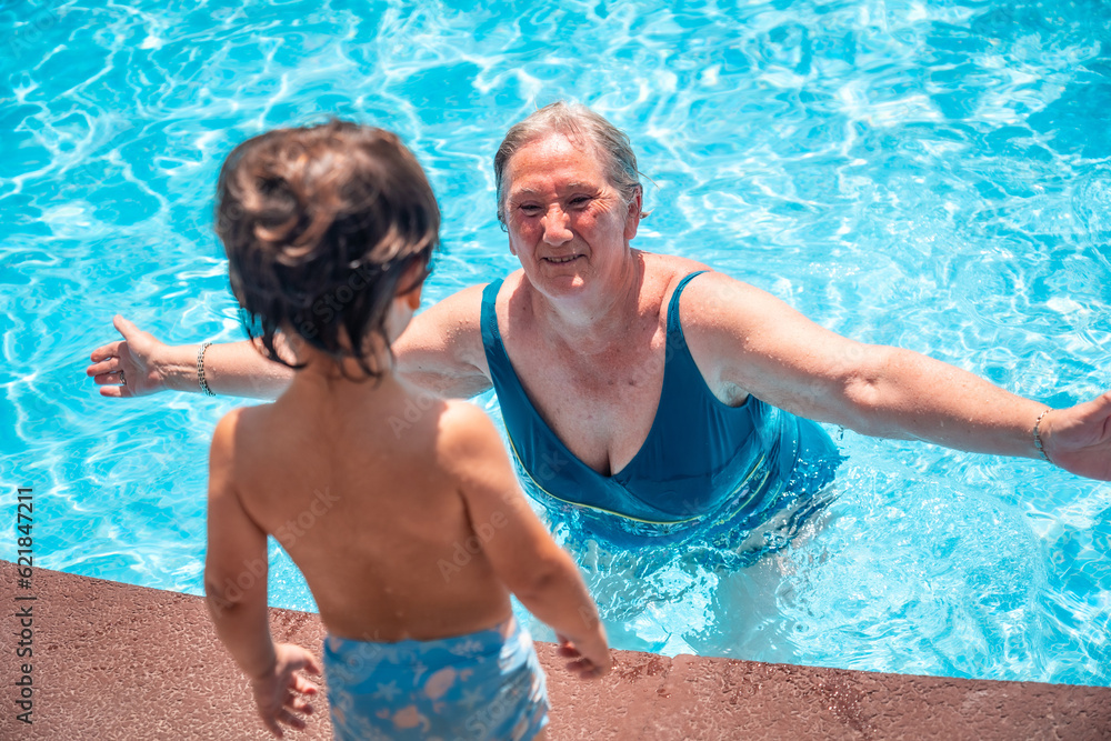 Mother and grandmother having fun with grandson in swimming pool on summer vacation, enjoying the water