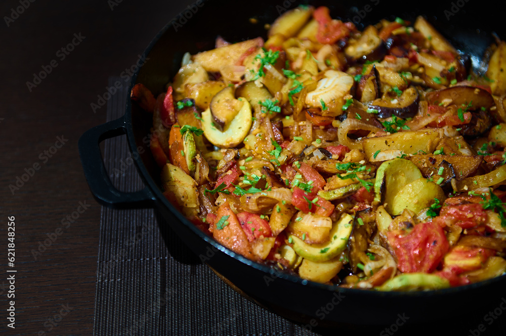 Freshly cooked vegetable stew of seasonal veggies in a cast-iron skillet, on a wooden background. Vegetarian tasty meal Freshly cooked vegetable stew of seasonal veggies in a cast-iron skillet, on a wooden background. Vegetarian tasty meal