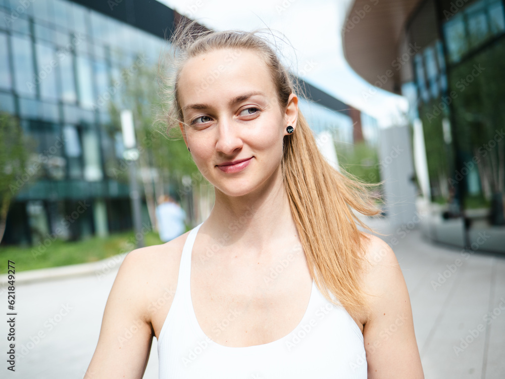 young blond woman outdoor in sunny summer day with urban background, looking at camera