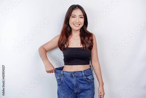 Diet and weight loss concept. A young Asian woman in oversized jeans isolated on a white background.